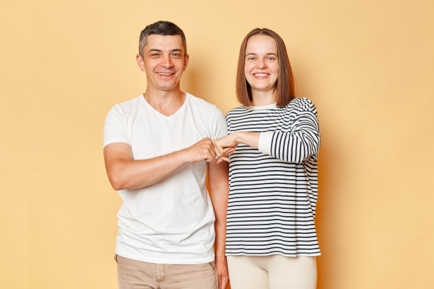 微笑的快乐的男人和女人穿着休闲服站在一起，用拳头碰着镜头，带着愉快的表情，很好地将米色背景隔离开来图片下载