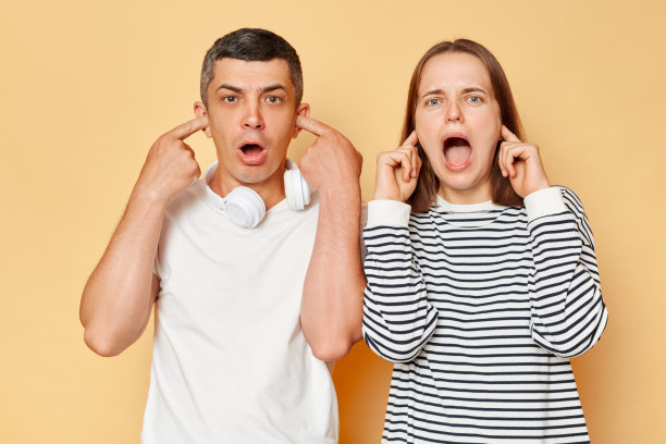 震惊，害怕，惊讶的男人和女人穿着休闲服，孤立地站在米色背景上，用手指捂住耳朵，不想听到什么。图片下载
