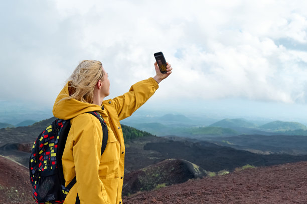 徒步旅行在欧洲大陆最高的火山-埃特纳。身着黄色雨衣的年轻女子在埃特纳火山全景的山顶自拍。图片下载