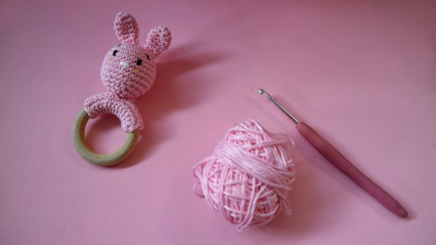钩针粉红兔拨浪鼓与棉纱和尼尔钩孤立在粉红色的背景。工艺的概念。手工婴儿玩具。粉色针织儿童兔。新生儿手工摇铃玩具。图片下载