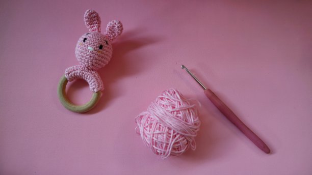 钩针粉红兔拨浪鼓与棉纱和尼尔钩孤立在粉红色的背景。工艺的概念。手工婴儿玩具。粉色针织儿童兔。新生儿手工摇铃玩具。图片下载