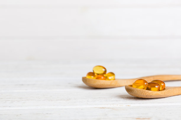 维生素欧米茄胶囊装在一个有色背景的勺子里。药片是健康的一餐。勺子上的红色软凝胶维生素补充胶囊图片下载