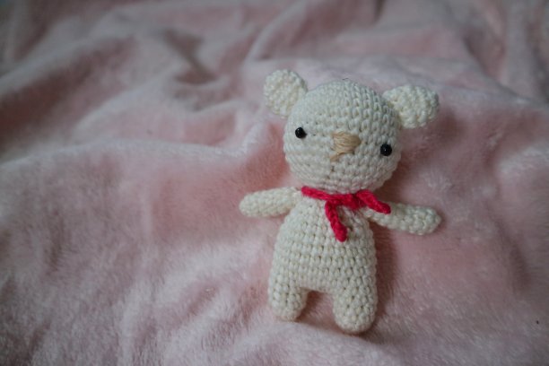 小白色的amigurumi熊毛茸茸的粉红色背景。手工编织的娃娃。艺术和工艺设计。图片下载