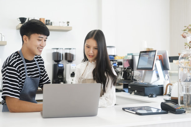 两个年轻的经理或店主在商店或咖啡馆的柜台上用笔记本电脑进行讨论。图片下载