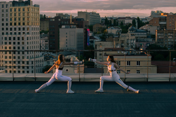 两名女子击剑运动员在以城市为背景的屋顶上练习。图片下载