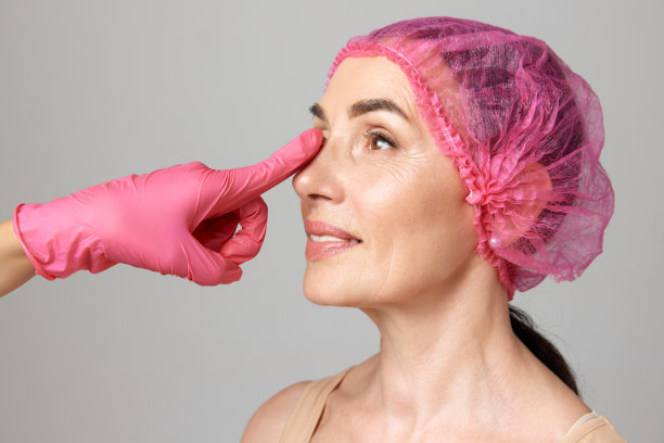 图为一位老妇人正准备接受整形手术，医生用粉色手套抚摸她的下巴。图片下载