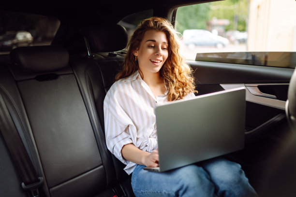 一位女商人在出租车上拿着笔记本电脑坐在汽车后座上工作图片下载