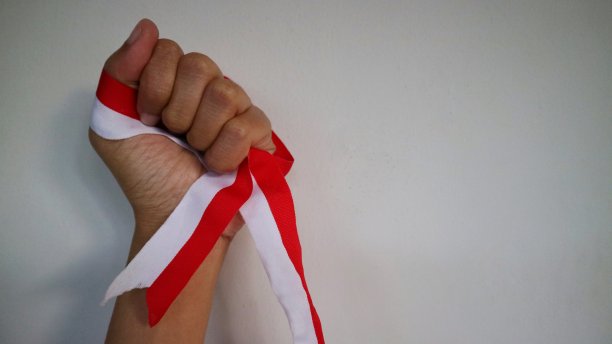 双手握拳，在空中战斗，庆祝印尼独立日。佩戴印尼红白丝带的独立标志。印尼独立日的概念。图片下载