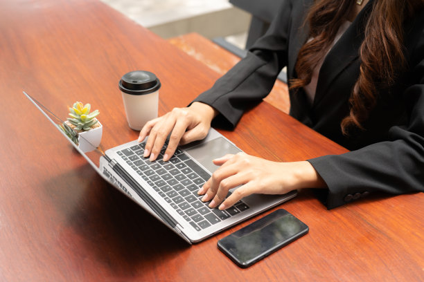 商务女性坐在办公桌前，带着专业的表情，手里拿着平板电脑，偶尔喝一口咖啡，专心地摆弄着手机。有效地处理她的任务。图片下载