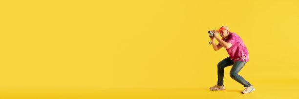 年轻人戴着明亮的帽子和t恤的横幅，在明亮的黄色背景下，在老式相机上拍摄过程。图片下载