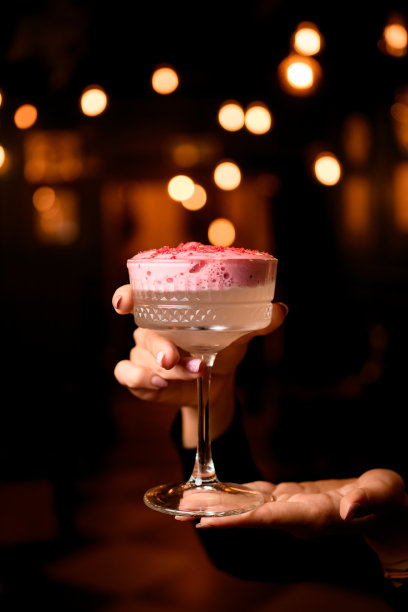 美丽的景色，酒杯与泡沫鸡尾酒装饰粉红色粉末在女性手中图片下载