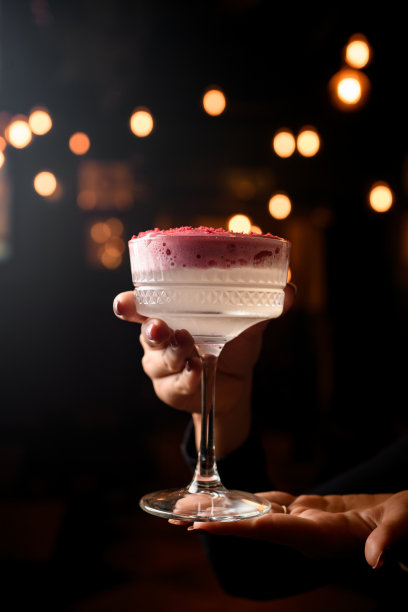 女性手中盛有泡沫鸡尾酒的高脚杯，上面装饰着粉红色粉末图片下载