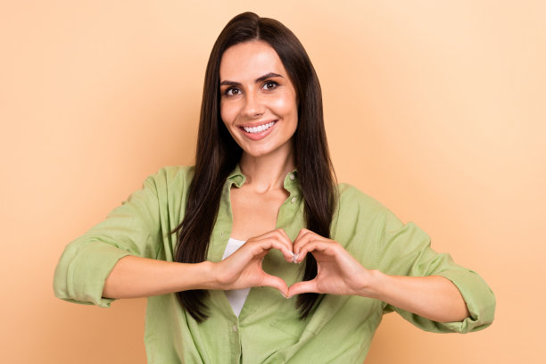 善良的好女孩的照片，直发，穿着绿色衬衫，手指显示心脏符号孤立在米色背景图片下载