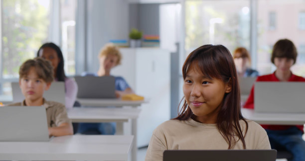 不同的青少年群体坐在教室里使用笔记本电脑。多民族青少年坐在桌上电脑前图片下载