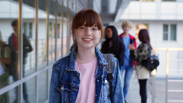 微笑的红发少女站在教学楼外看着镜头图片下载