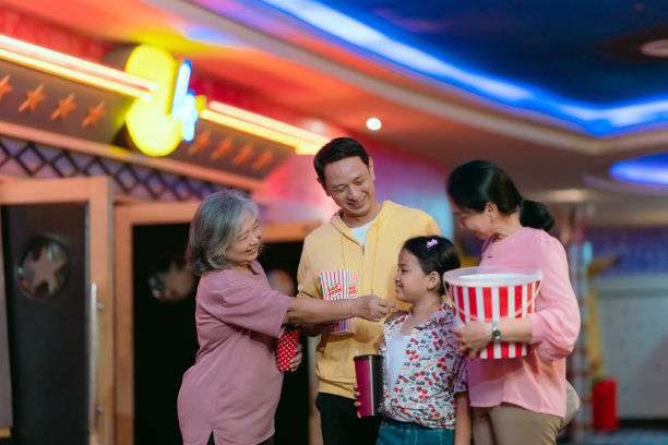 家人，父母，孩子和奶奶拿着爆米花，喝着水，在电影前愉快地聊天。图片下载