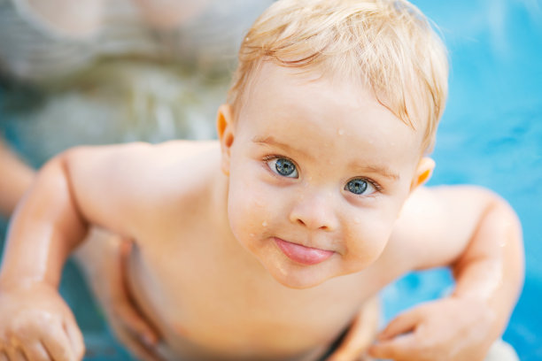 小红发男孩用手托着在泳池里洗澡，婴儿在水里游泳，夏日休闲图片下载