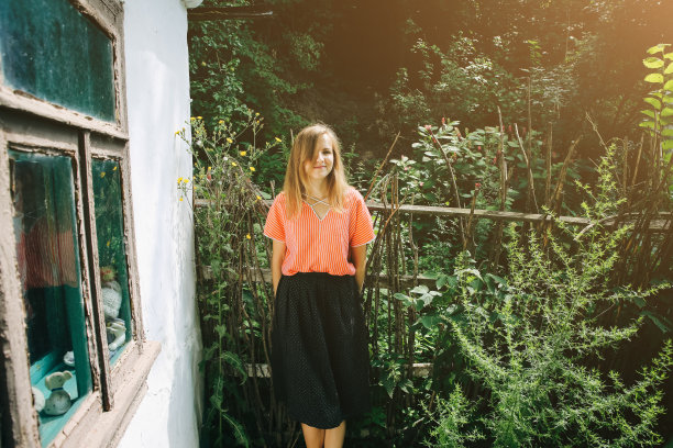 穿着漂亮复古衣服的女人站在老木屋旁边。夏日的乡村风格照片。谷仓或农场附近的院子。图片下载