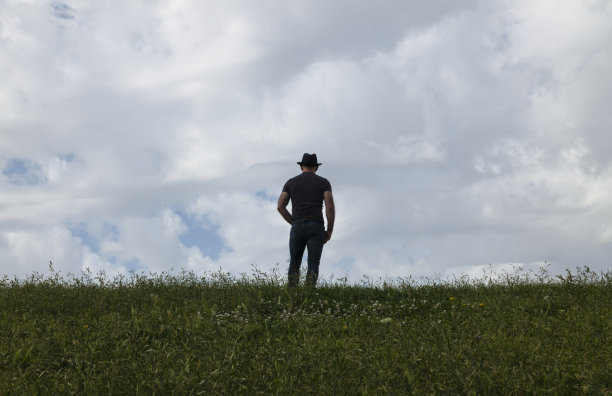 多云的天空下，戴着帽子的成年男子的后视图图片下载