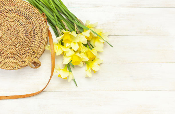 时尚手工制作的天然有机圆藤袋，黄色水仙或水仙花在轻木背景平lay。来自巴厘岛的时尚竹袋Ecobags。夏季时尚概念俯视图图片下载