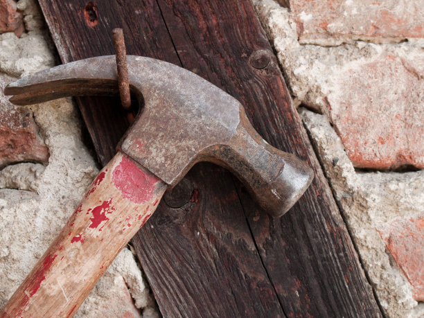 自然光下石墙钉子上挂着的锤子特写图片下载