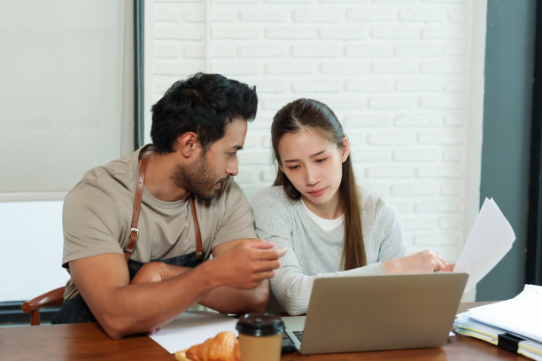 年轻英俊的印度夫妇和亚洲女人是一家小公司的咖啡师和店主。坐在桌边，商量咖啡馆的管理。并准备在网上销售，在笔记本电脑前图片下载