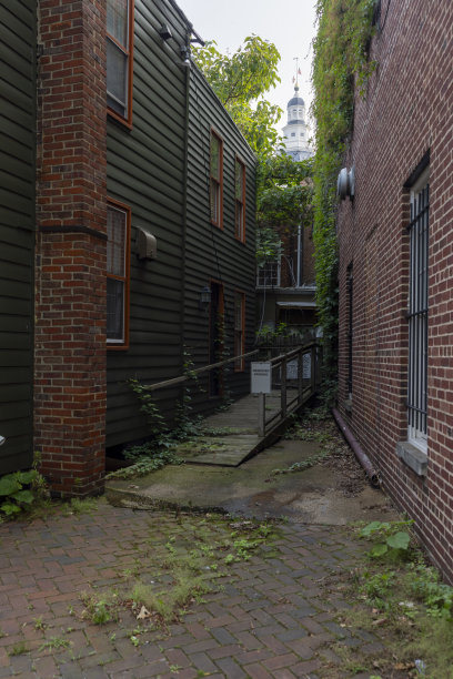 在烟雾缭绕的天空下，马里兰州安纳波利斯的马里兰州议会大厦位于老房子之间的黑暗小巷中图片下载