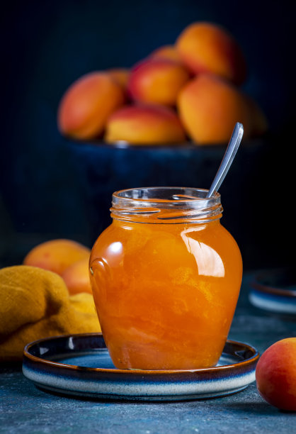 杏果酱或配置在玻璃罐与勺子，新鲜水果在蓝色的桌子背景图片下载