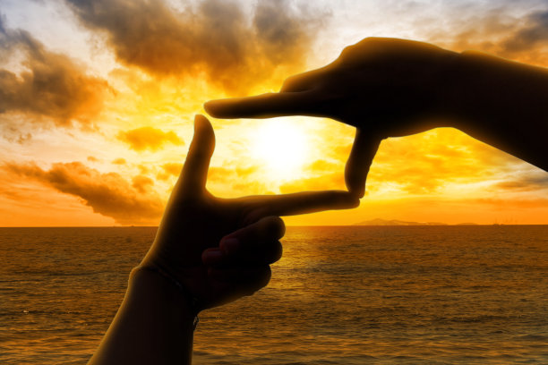 年轻女子手挽成方形，太阳在地平线上。图片下载