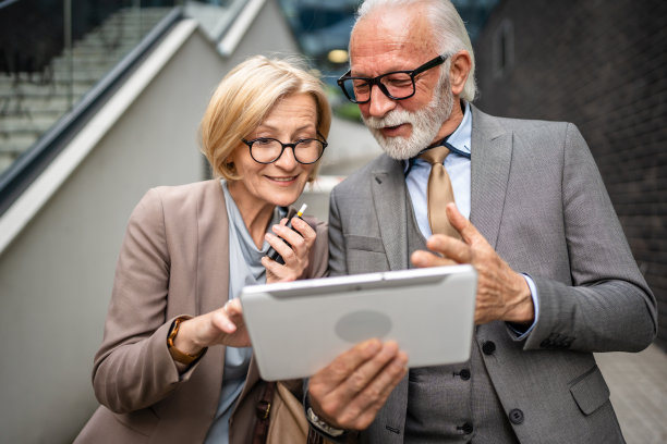 穿着西装的年长男子和成熟的金发女子作为商业伙伴，夫妻朋友或同事交谈，手持数码平板电脑浏览互联网，查看数据，交换意见，复制空间图片下载