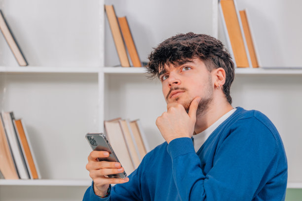 年轻男学生带着手机或智能手机，脸上带着怀疑的表情图片下载