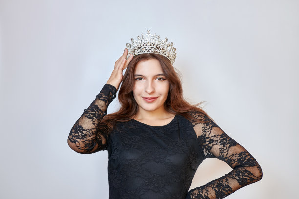 一个穿着黑色连衣裙的漂亮女孩用手捧着一顶皇冠。选美比赛的概念。胜利者的情绪。图片下载