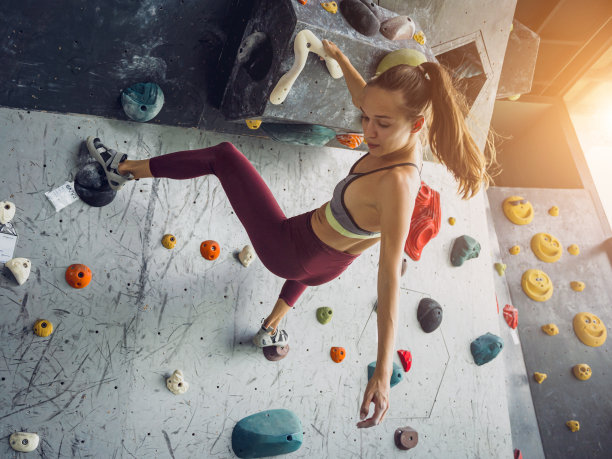一位强壮的女攀岩者用彩色的握把和绳索爬上一堵人造墙。图片下载