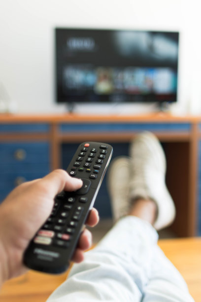 一只手拿着电视遥控器的垂直照片，而他的脚放在桌子上。图片下载