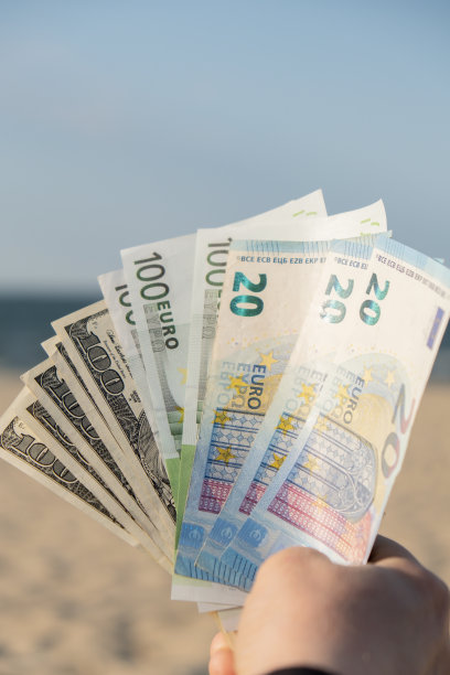 一名无法辨认的女子在沙滩上展示现金欧元和美元钞票。概念理财为度假攒钱。旅游度假费用。额外的钱图片下载