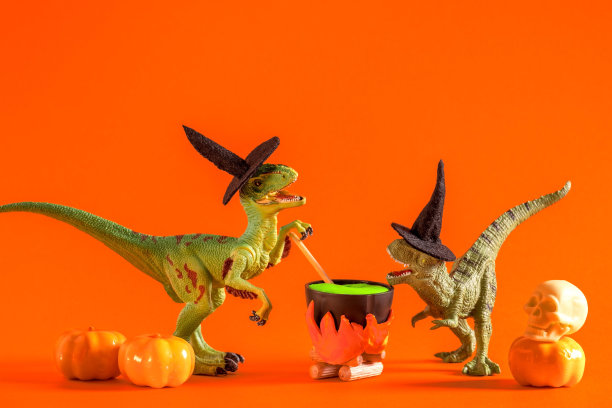 两只戴着女巫帽的搞笑恐龙正在橙色背景的锅里酿造药水。万圣节贺卡。图片下载