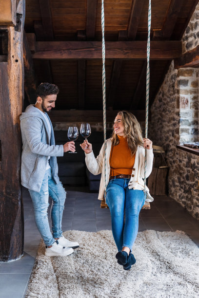 一对夫妇在他们乡村住宅的阁楼上的秋千上喝着一杯酒的垂直照片，一对年轻夫妇在一个浪漫而快乐的夜晚的生活方式。图片下载