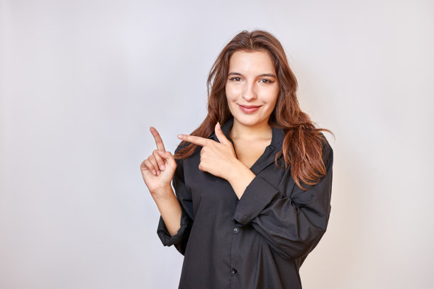 一个穿着黑色连衣裙的漂亮女孩用手指着背景上可能的题词。图片下载