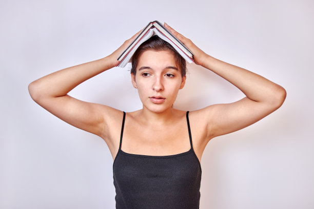 这个女孩把打开的书顶在头上。艰苦训练的概念。图片下载