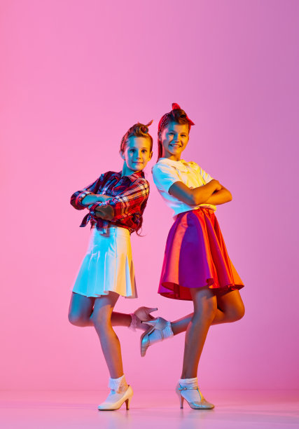 美丽，时尚的女孩，孩子们穿着复古的衣服，在霓虹灯的粉红色工作室背景下跳着林迪舞图片下载