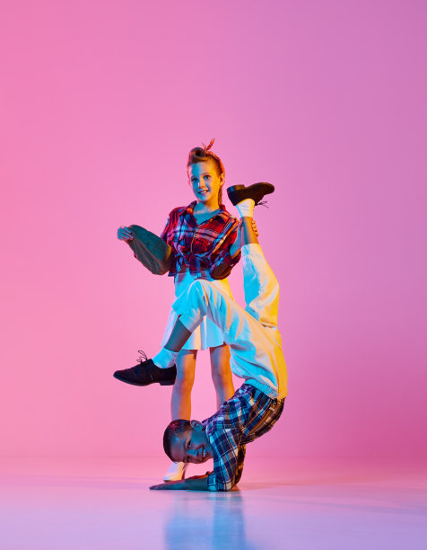 的灵活性。时尚活泼的孩子们，女孩和男孩穿着复古风格的衣服，在霓虹灯的粉红色工作室背景下跳舞图片下载