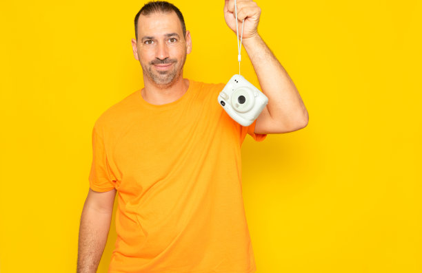 40多岁的西班牙裔男子，留着胡子，挂着照相机，孤零零地站在黄色的摄影棚背景上。图片下载