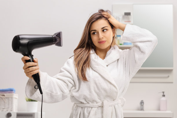 穿着浴袍的年轻女子在浴室里吹头发图片下载
