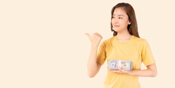 快乐的年轻亚洲妇女拿着美元钞票，指着黄色背景上孤立的空间。快乐的亚洲女士拿着美元，微笑的女孩赚了很多钱或中了彩票图片下载