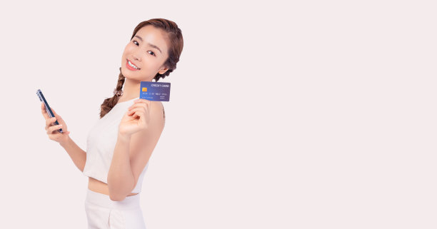 年轻的亚洲女士用手机拿着信用卡看着相机孤立在柔和的白色背景和复制空间微笑的年轻女孩通过手机用信用卡在线购物图片下载