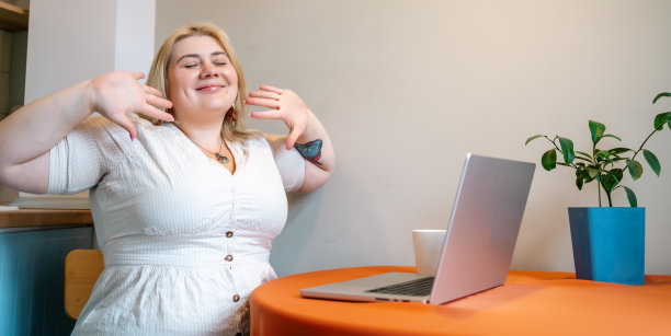 快乐微笑的大码女人坐在桌子上用笔记本电脑享受她的咖啡休息时间在家里工作的地方图片下载