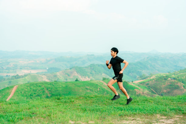 年轻的亚洲男子跑步，穿着黑色运动服，在一条大山路上跑步，凉爽的早晨，风车，和天空的背景。图片下载
