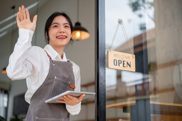 一个漂亮的亚洲女咖啡店工作人员站在门口，手里拿着一个平板电脑图片下载