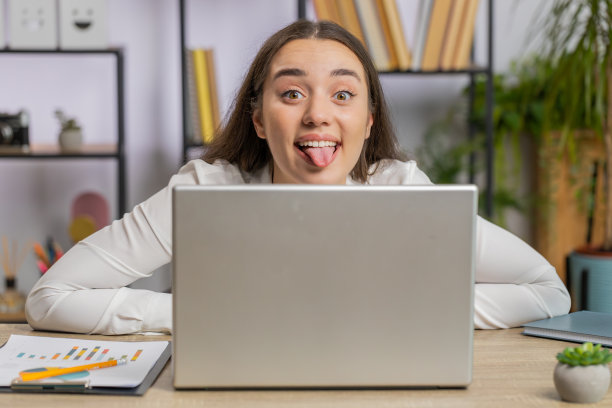 办公室女商人躲在笔记本电脑后面，做着滑稽的傻脸，胡闹，不尊重图片下载