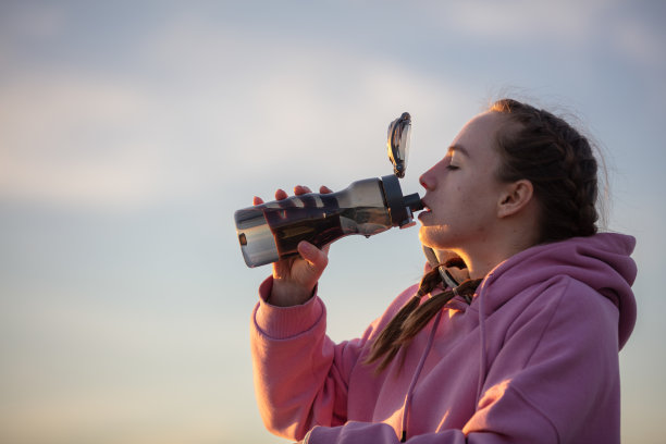 日落时分，年轻的女运动员正在喝水。图片下载